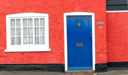 A colorful cottage in a British village with red walls and a blue door